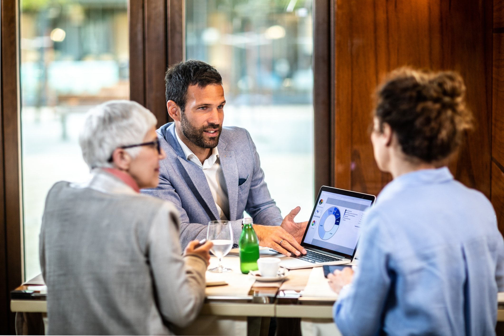 Three people sitting around a table with a laptop on the table.