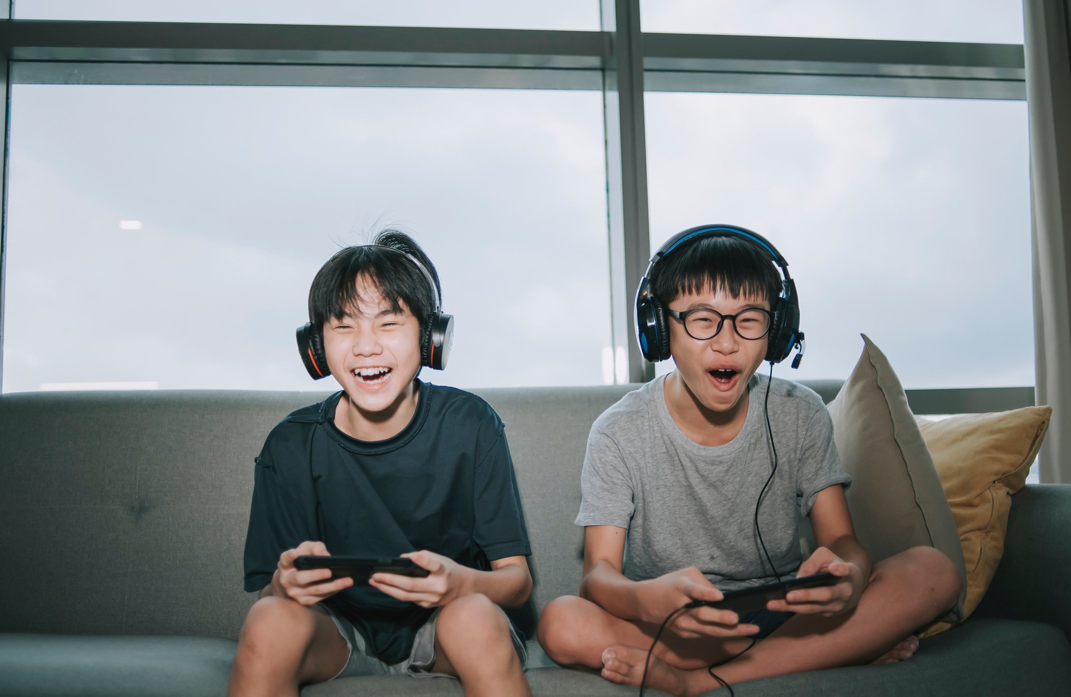 Two kids happily play video games sitting on a couch