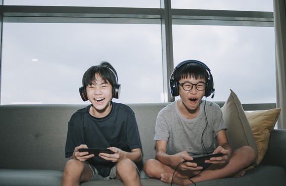 Two kids happily play video games sitting on a couch