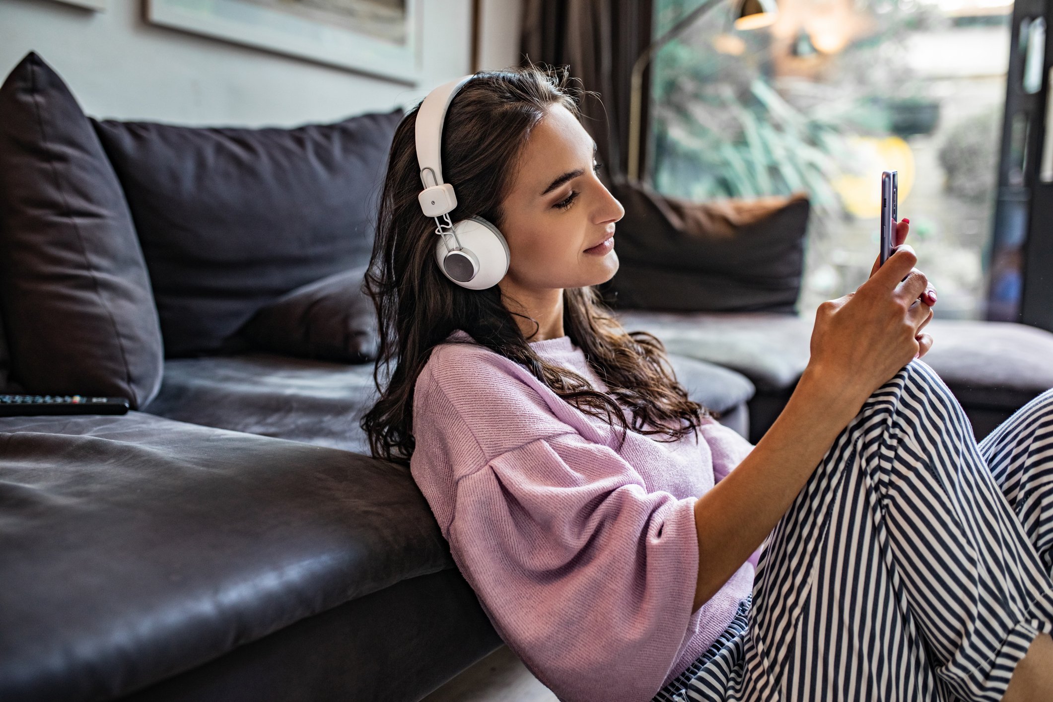 Person sitting on living room floor with over-the-ear headphones on and phone in hand.
