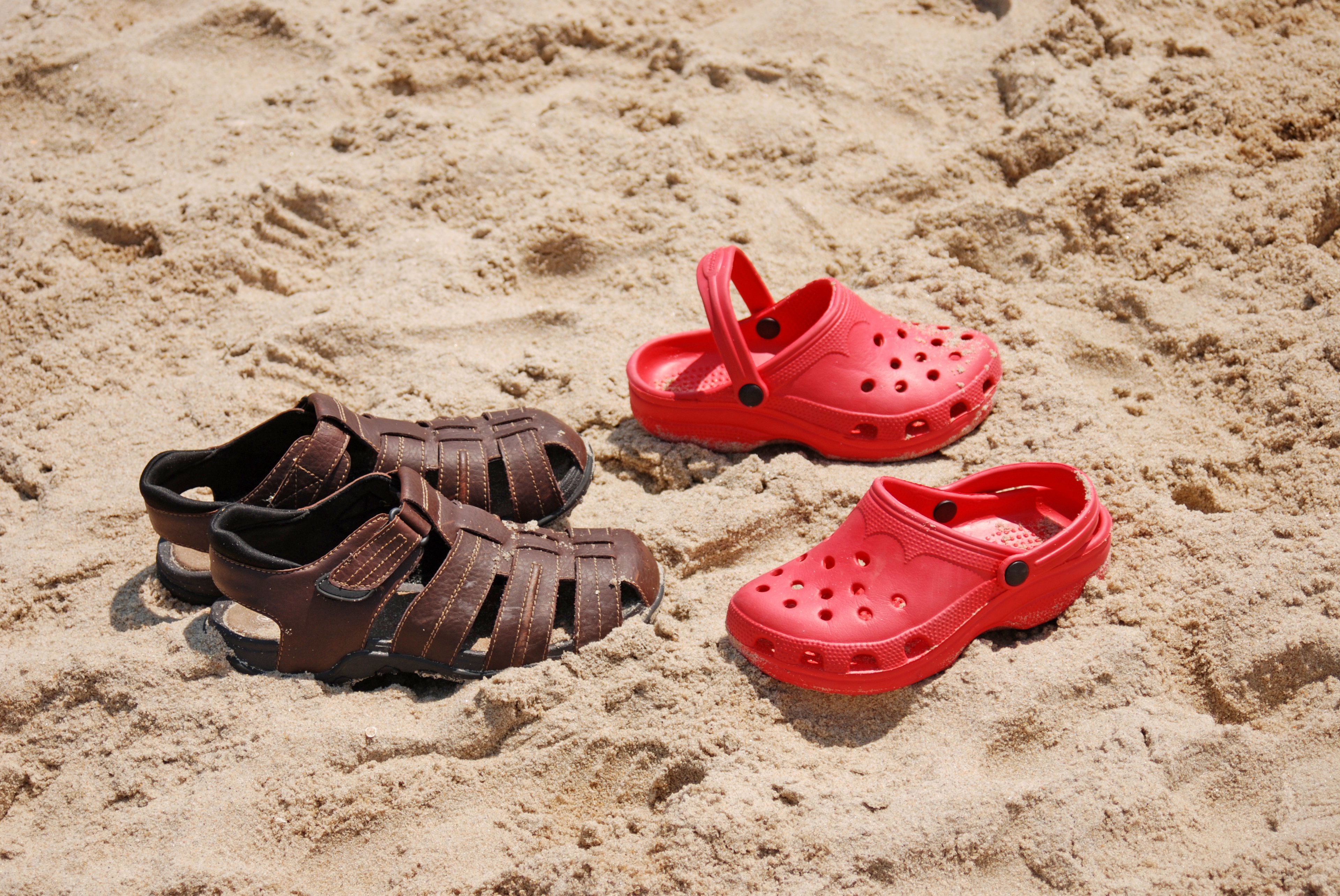 A pair of Crocs and a pair of sandals on the beach.