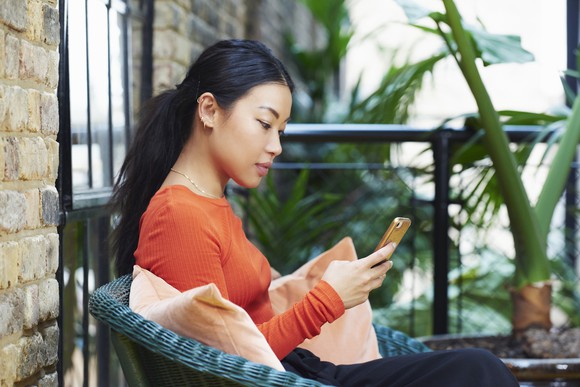 A person sits on a porch looking at their smartphone.