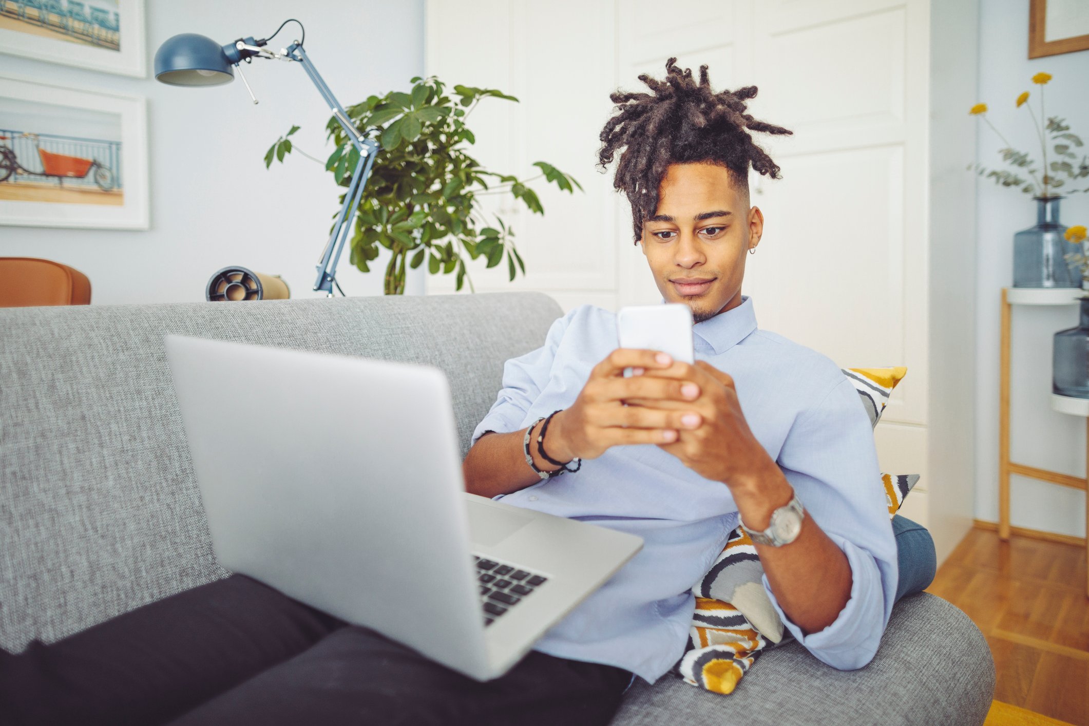 A person looks at a smartphone while balancing a laptop on a home couch.