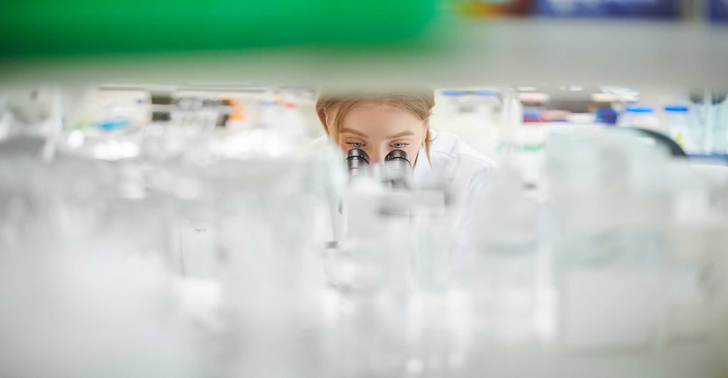 A scientist peers through a microscope in a cluttered biomedical research laboratory.