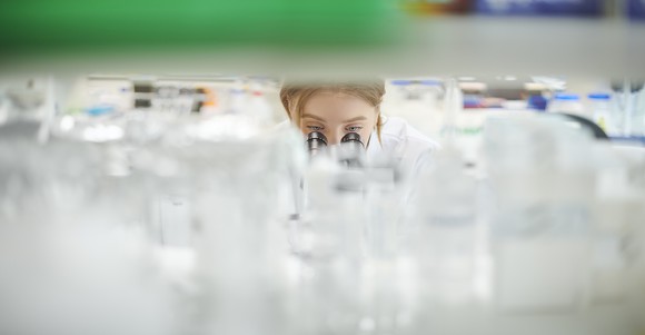 A scientist peers through a microscope in a cluttered biomedical research laboratory.