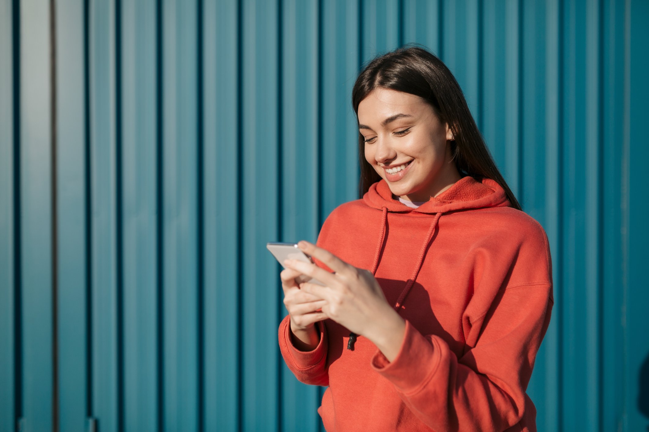 A smiling person standing outside looking at their cell phone.