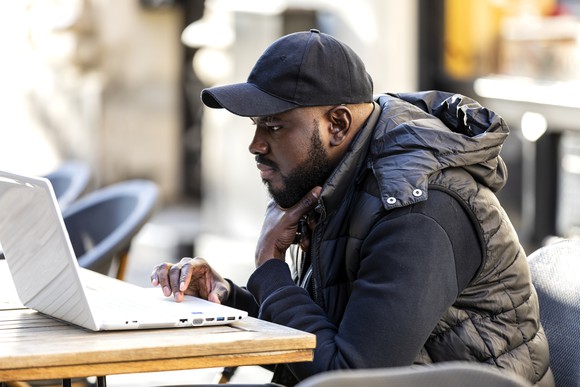 A person sits outside looking at a laptop.