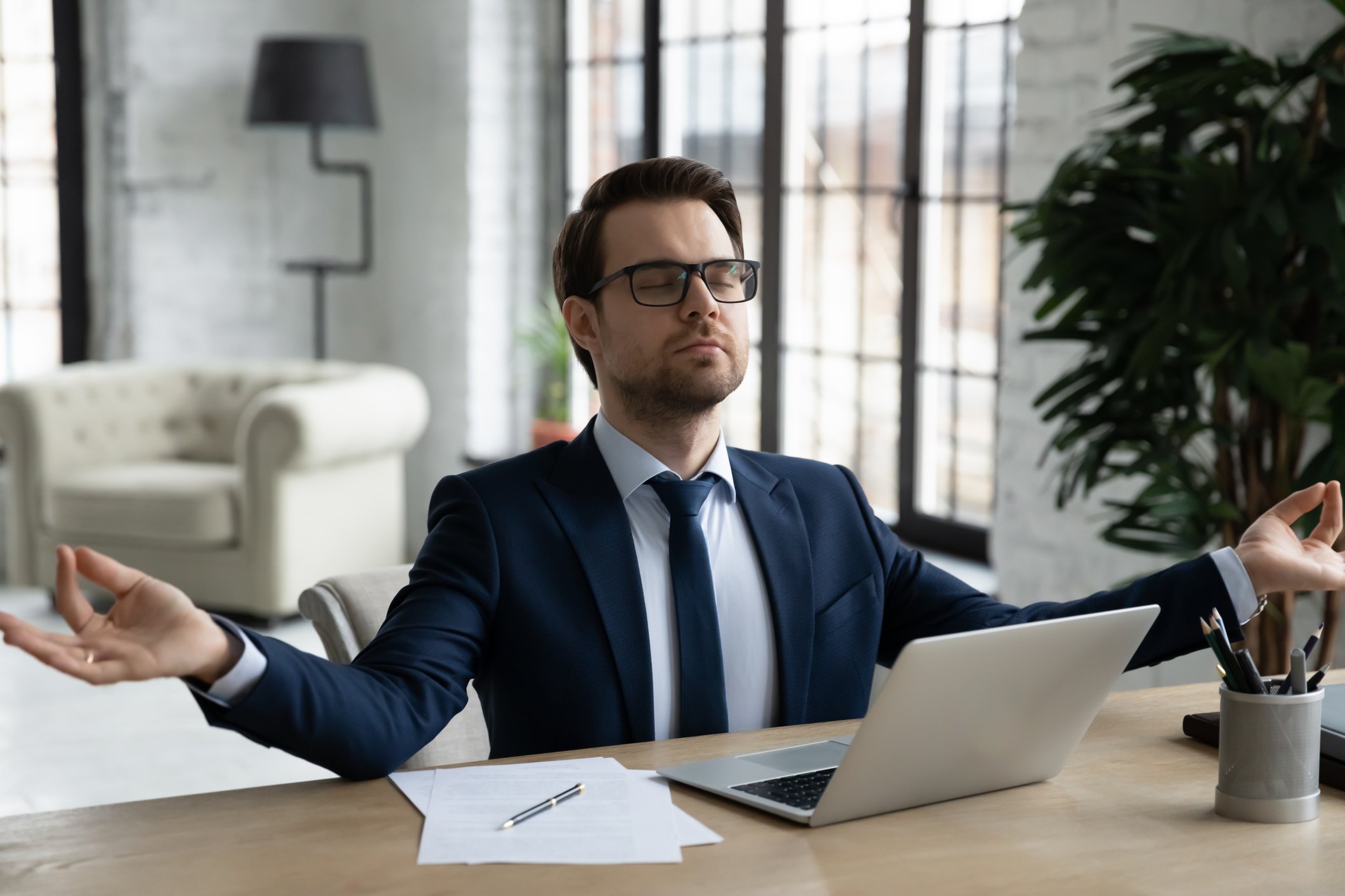 A person wearing a suit and tie meditating at their desk.