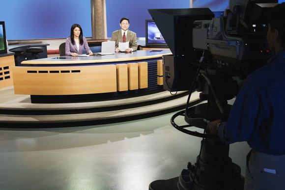 Television news broadcast desk with two announcers, and camera.