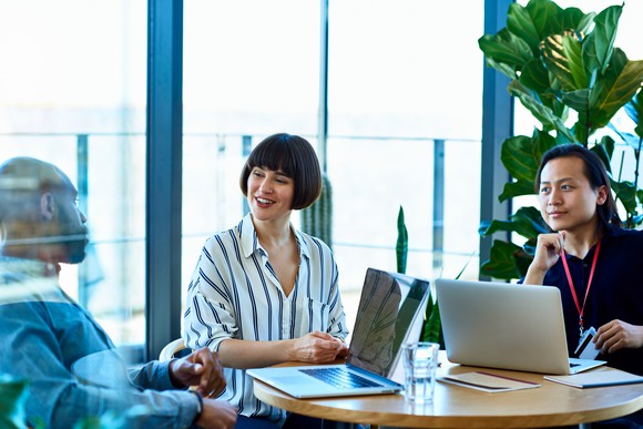 Three employees sitting around a table with computers.