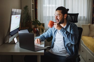 A person holding a mug and looking at a computer.