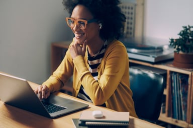A happy woman works on a laptop.