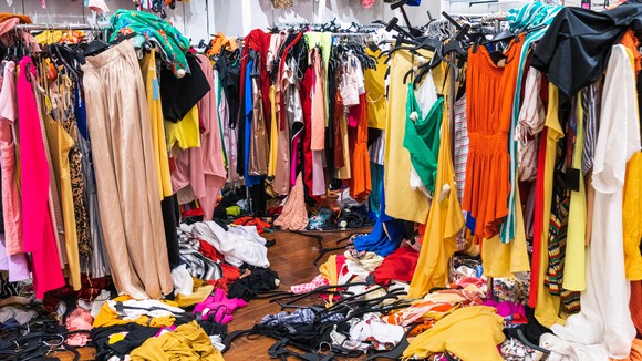 A jumble of clothes on clothes racks and floor
