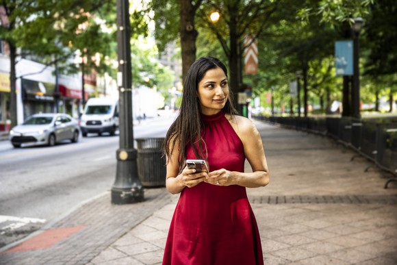 A woman standing on a sidewalk, holding a phone, trying to determine which way to go. 