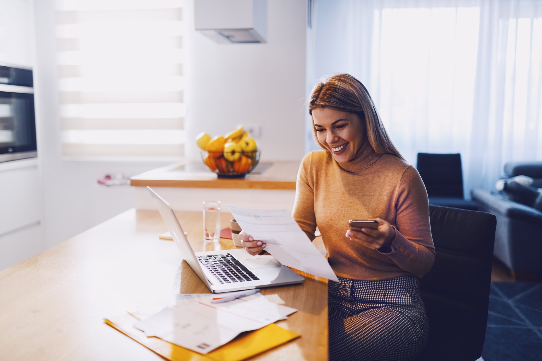 Younger adult smiling as she reviews paperwork at home.