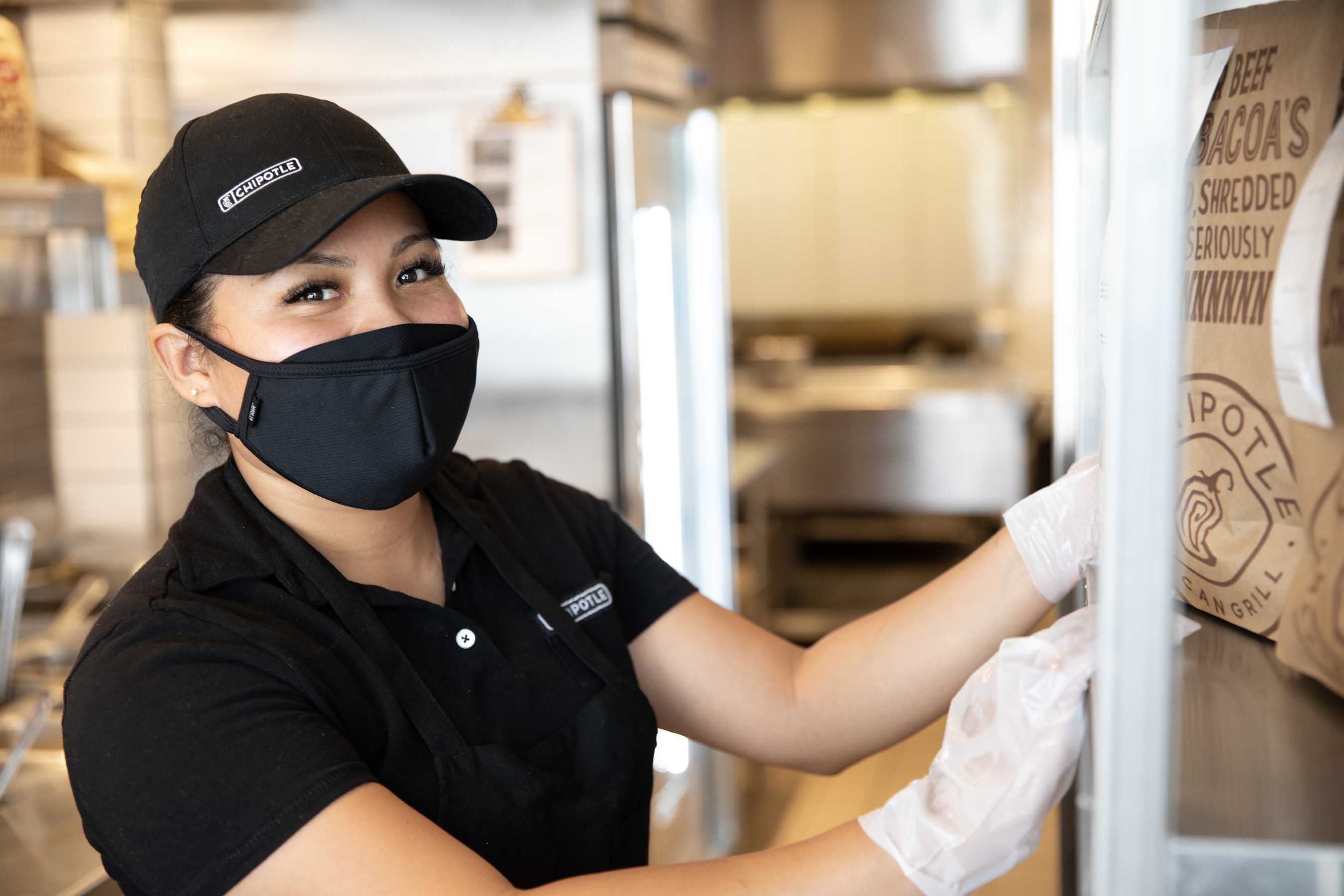 A Chipotle worker reaches for a carryout bag while working in a restaurant.