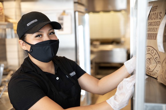 A Chipotle worker reaches for a carryout bag while working in a restaurant.