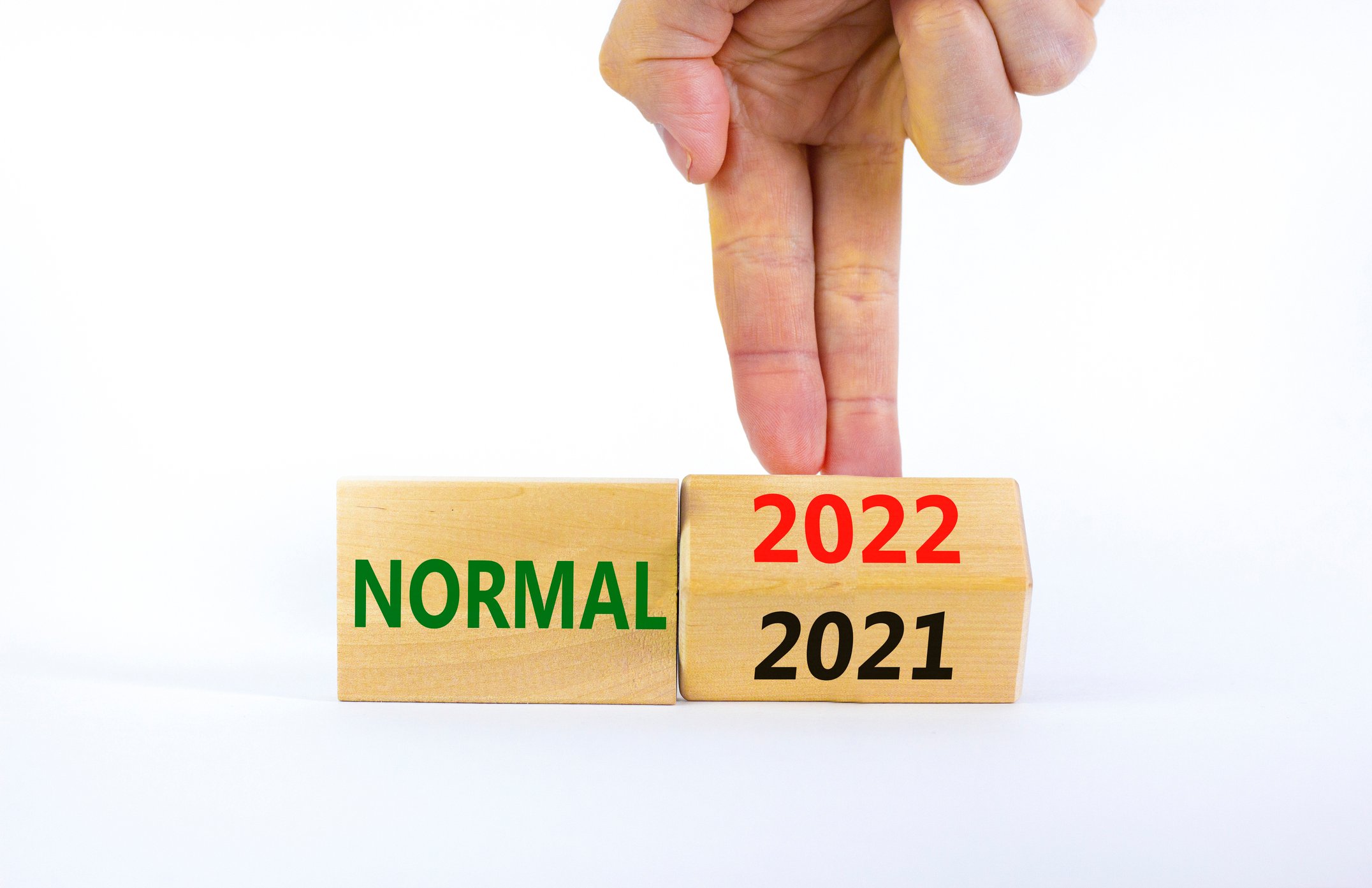 A wood block with "normal" printed on it with fingers turning another wood block from 2021 to 2022.