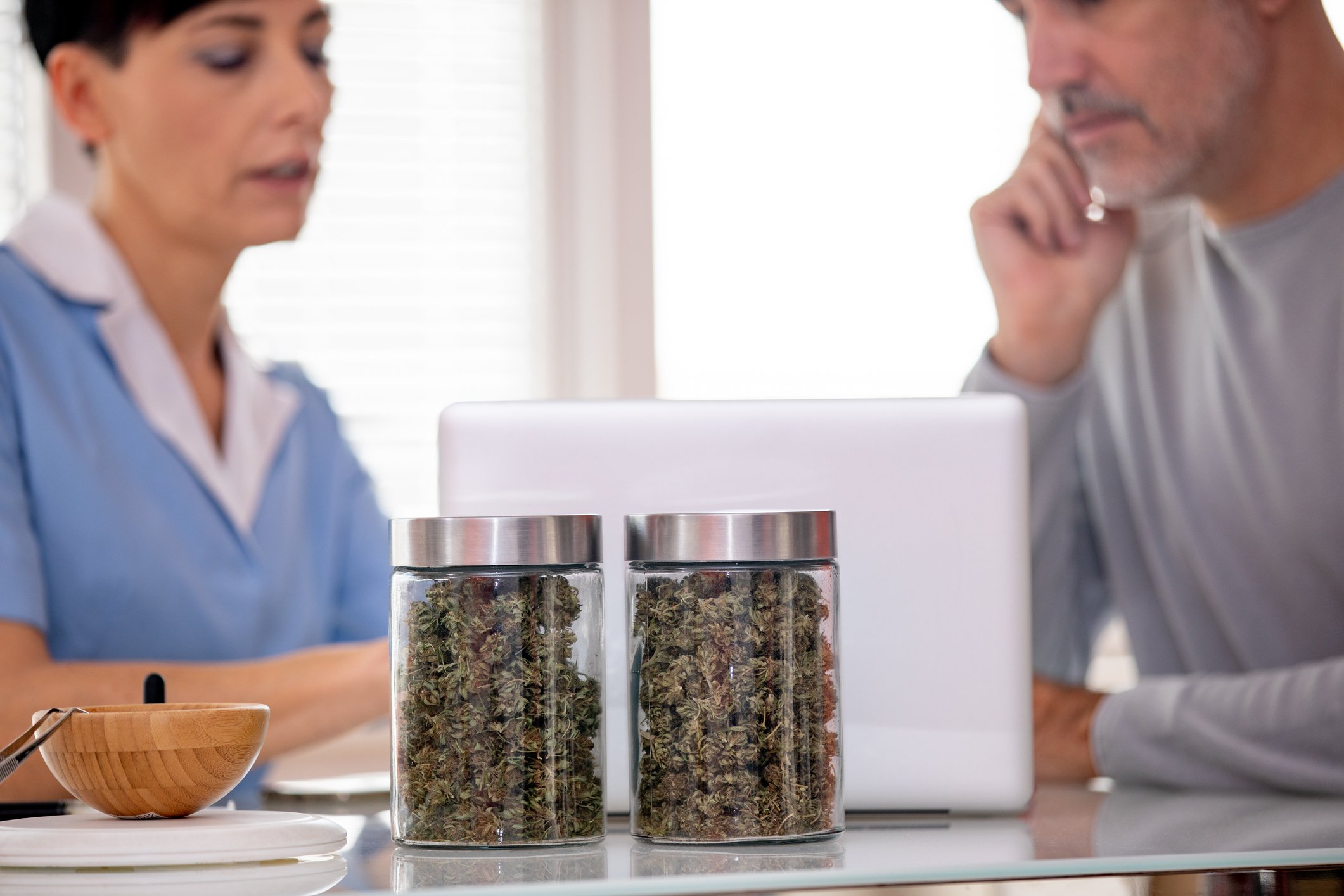 Two people looking at a laptop with two canisters containing cannabis in front of the laptop.
