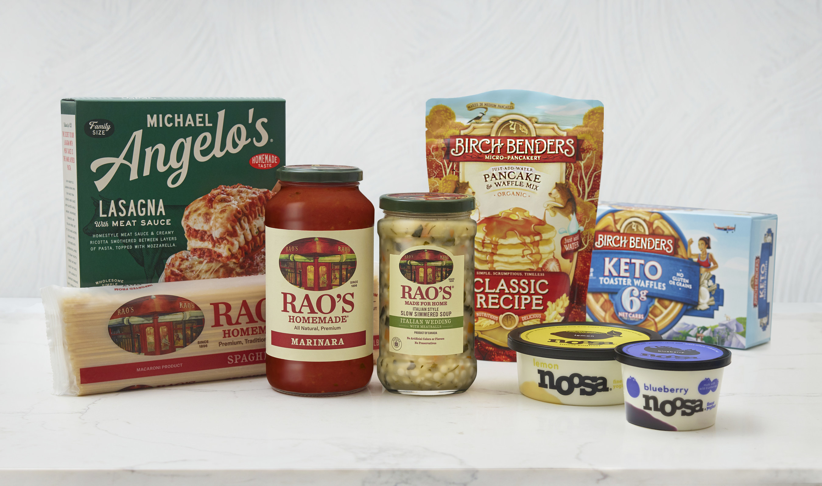 Boxes and containers from Sovos Brands, including spaghetti, lasagna, pasta sauce, yogurt, and pancake mix sit on a white table