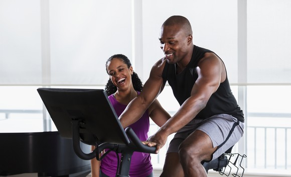 person riding a stationary bike while someone stands beside