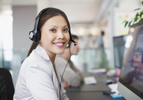 Worker smiles while wearing a headset and completing tasks online.