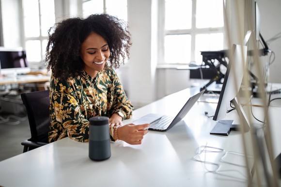 Person sitting at a desk in front of a laptop and holding a debit/credit card. 