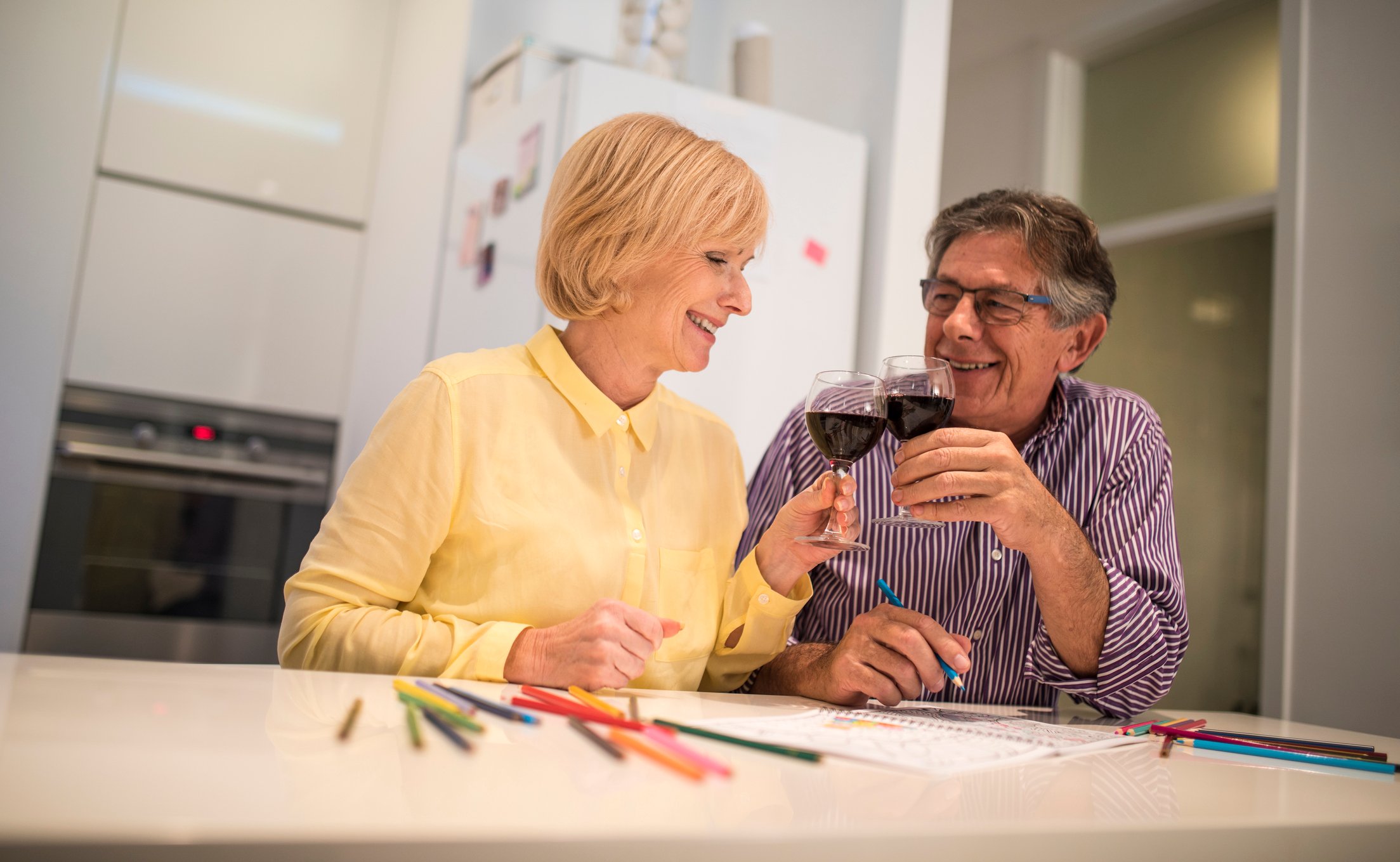 Two smiling, middle-aged adults clinking wine glasses together.