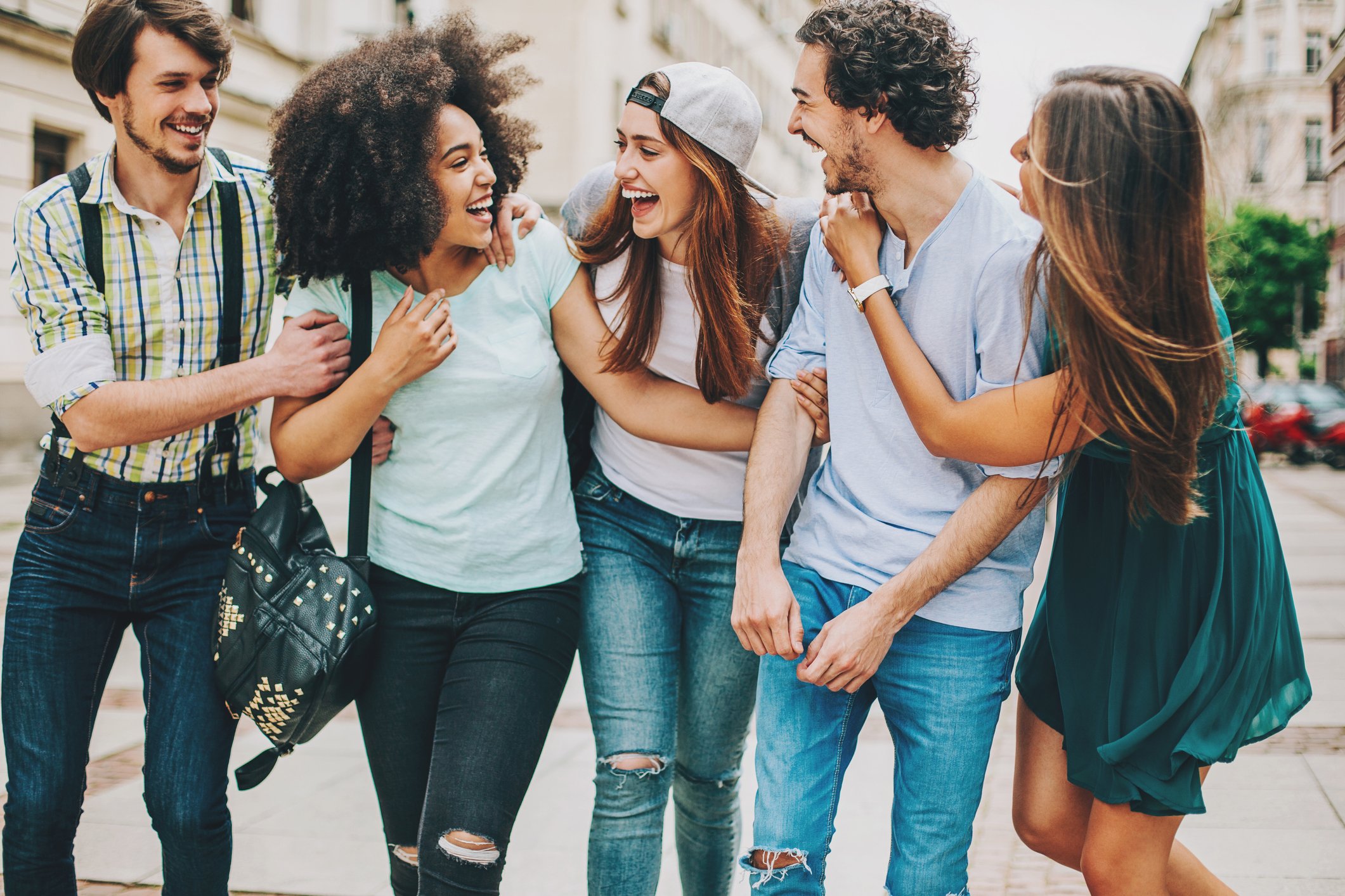 A group of young firends, laughing and talking on a city street.