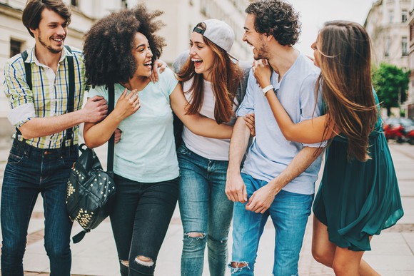 A group of young firends, laughing and talking on a city street.