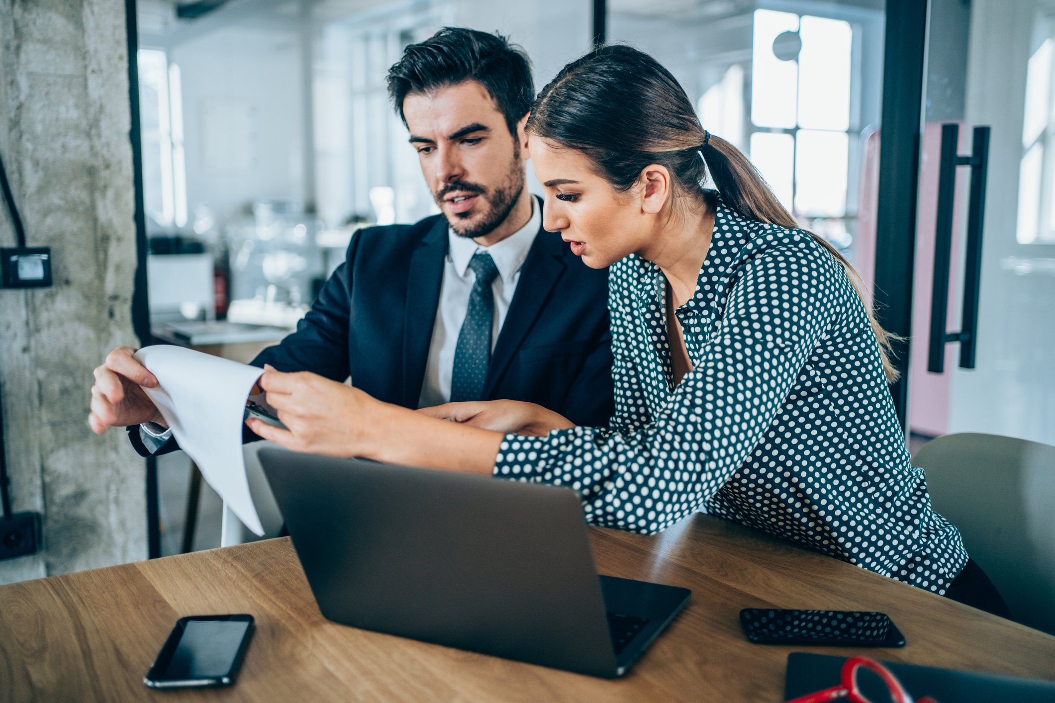 Two people study a document as they sit in front of a laptop in an office.