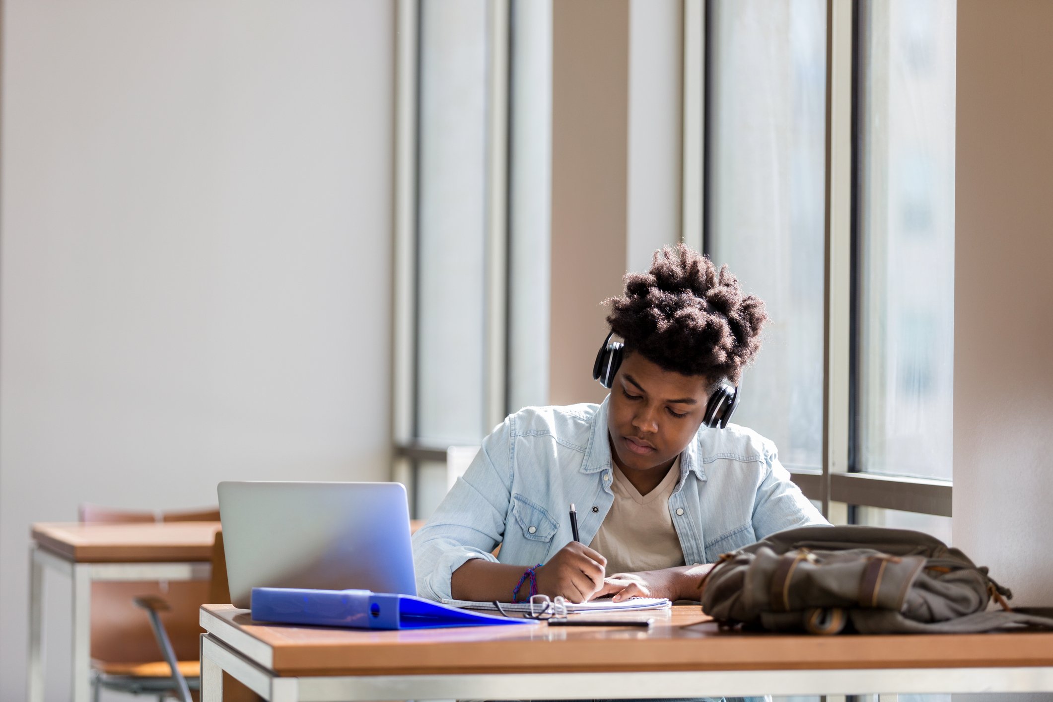 A student wearing headphones sitting at a desk writing.