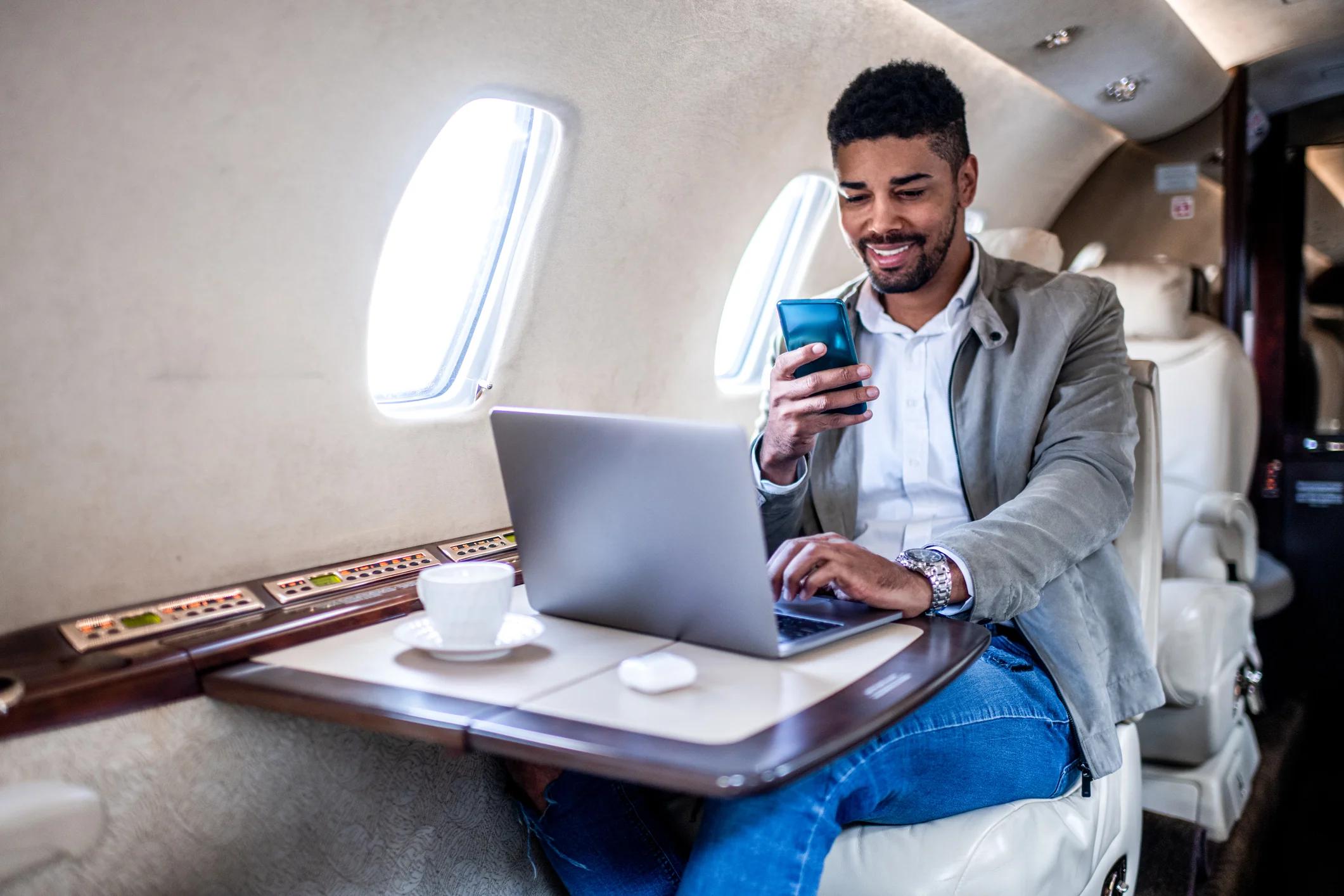 Person in private jet using computer amd looking at smartphone.