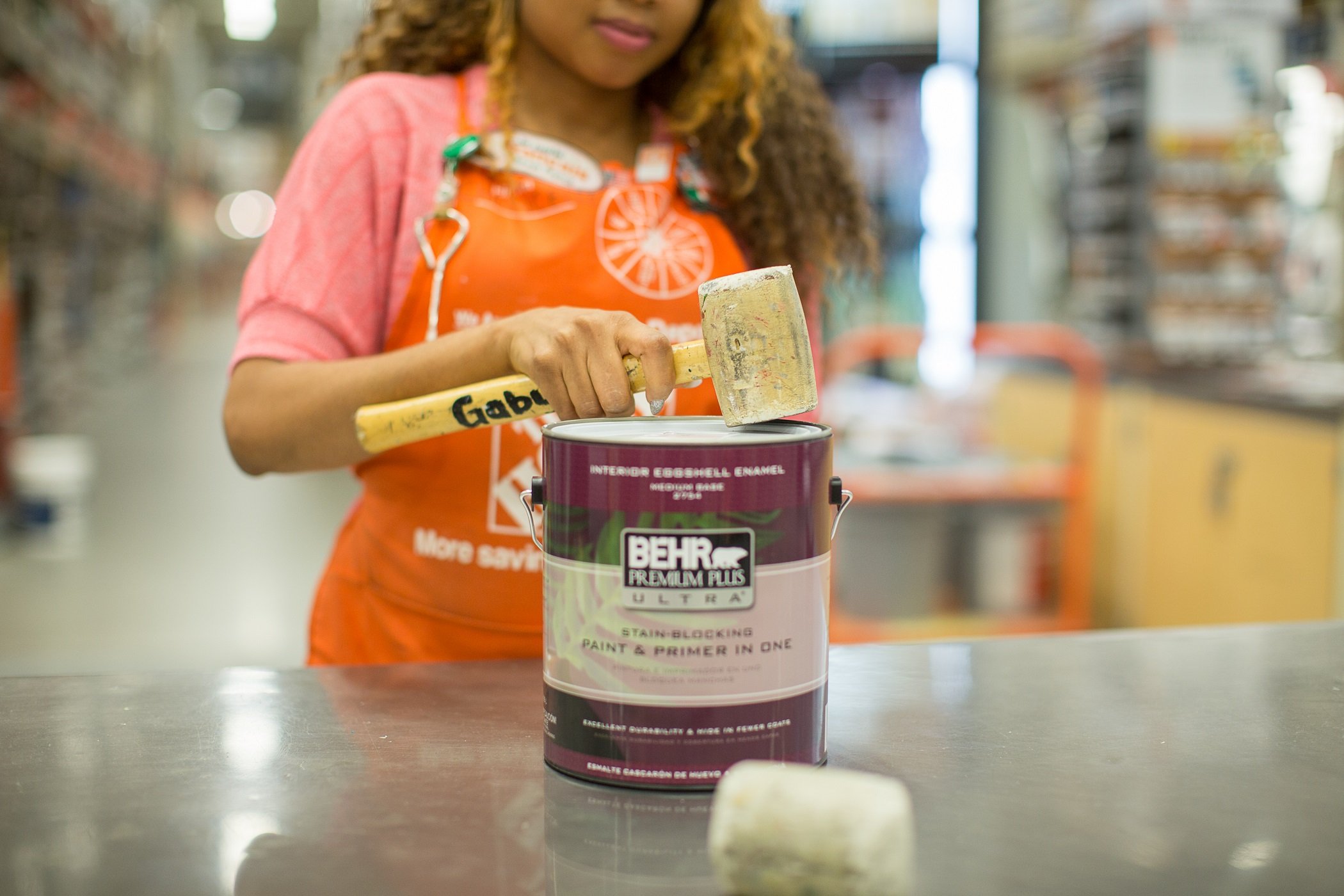 A Home Depot employee uses a rubber mallet to seal the lid on a paint can sitting on a table in a Home Depot store.
