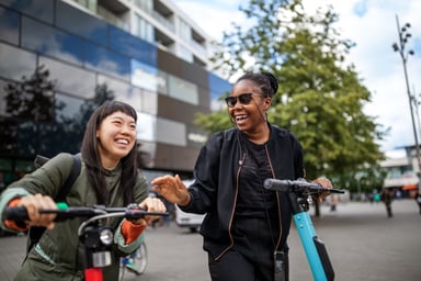 Two smiling people riding electric scooters