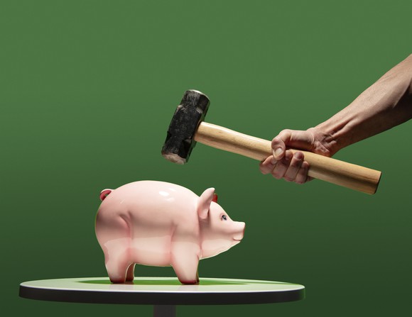 An arm holding a sledge hammer above a piggy bank.