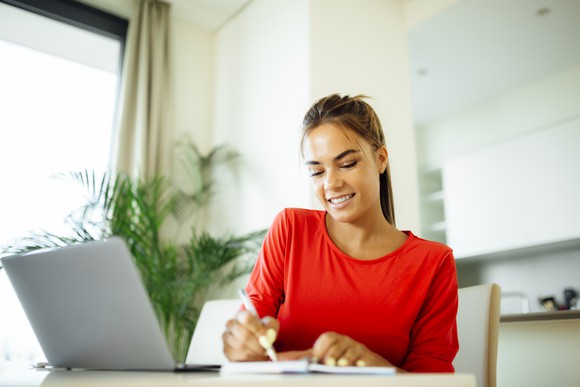 Investor taking notes, while sitting at her computer.