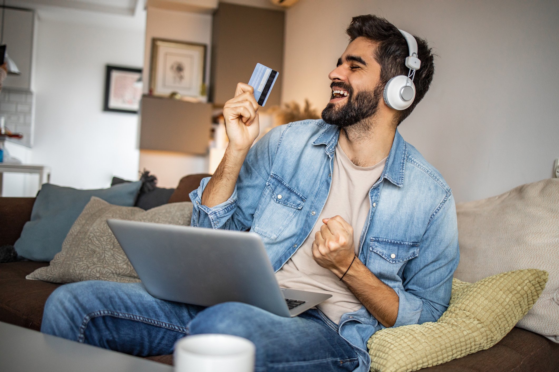 Young guy pumps his fist listening to headphones and holding a credit card. 
