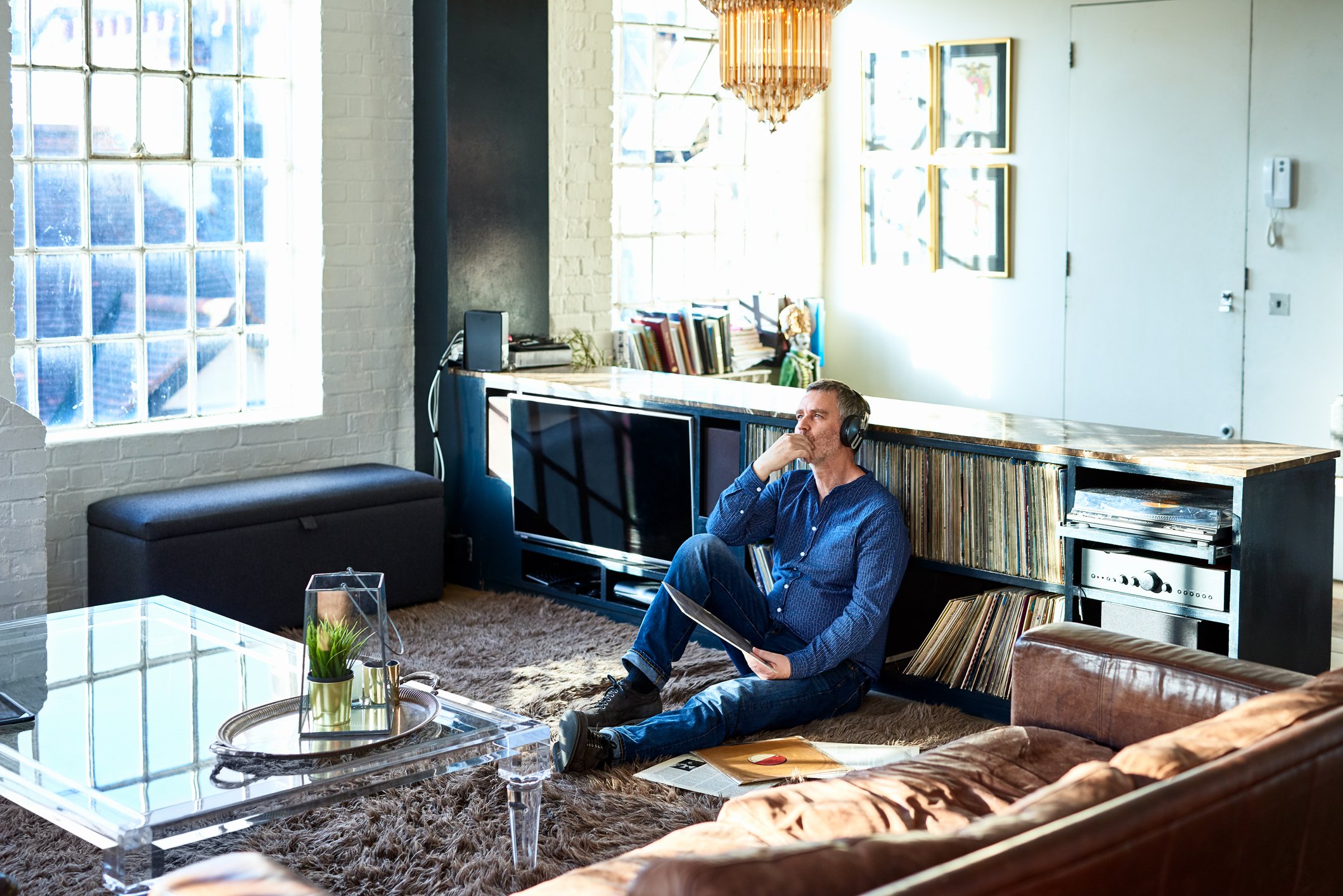 Person in deep thought wearing headphones and sitting on the floor in a living room.