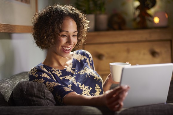 A person holds a tablet in one hand and a coffee mug in the other.