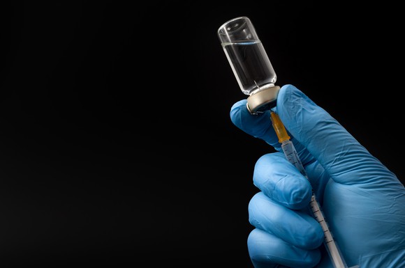 Gloved hand filling a syringe from a vial.