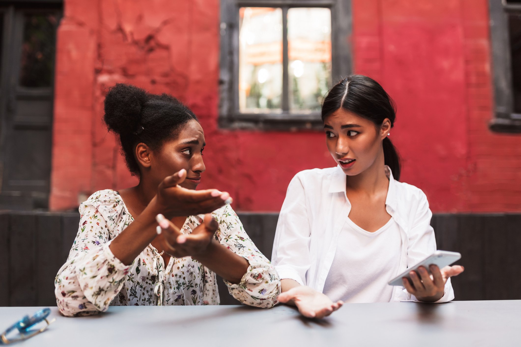 Two people, one with smartphone, talking at a table.