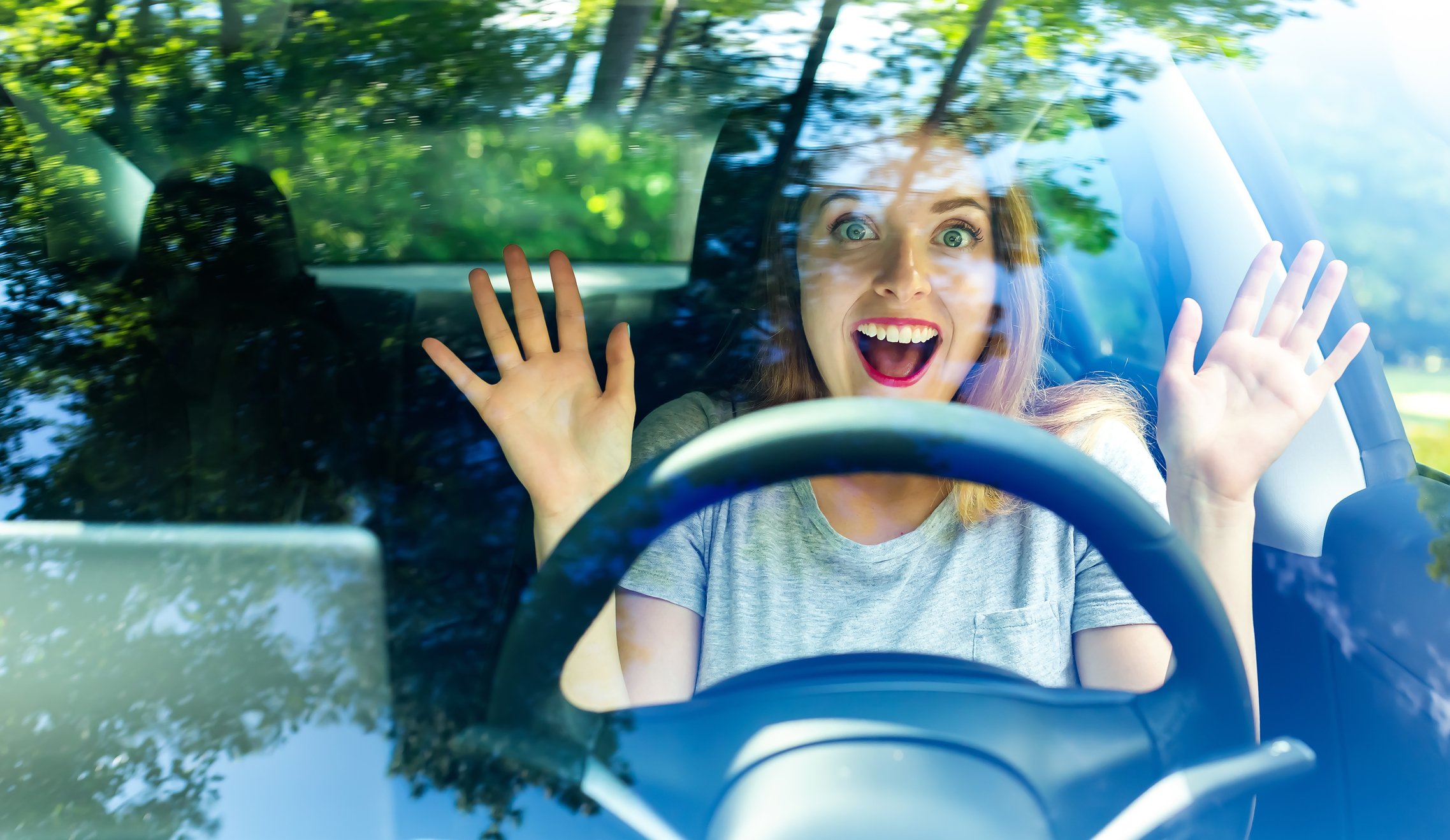 A person behind the wheel of a car smiling with their hands in the air.