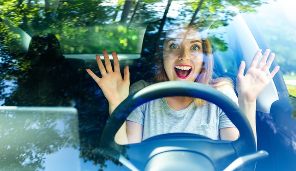 A person behind the wheel of a car smiling with their hands in the air.