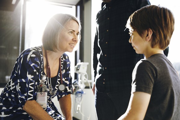 Smiling doctor talks to a young patient beside a parent in an office.