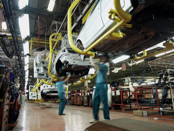 Workers at a modern car factory putting the finishing touches on vehicle undercarriages.