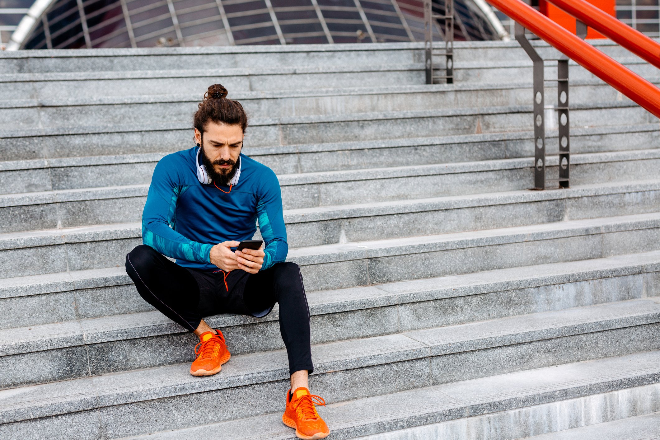 Person sitting on steps, looking at phone, wearing athletic clothing.