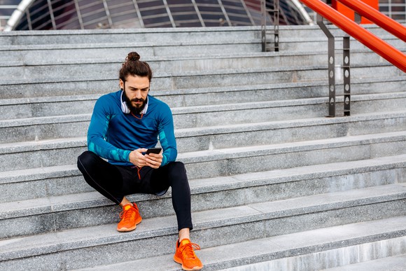 Person sitting on steps, looking at phone, wearing athletic clothing.