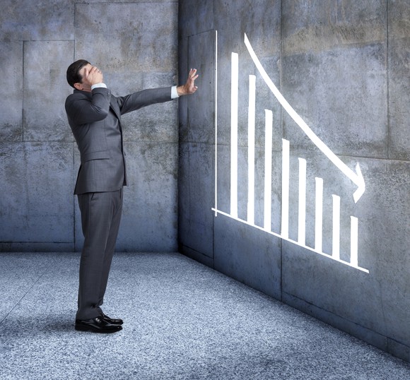 A businessman looking away from a downward trending graph.