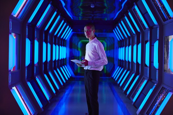 Man with laptop standing in spaceship corridor.